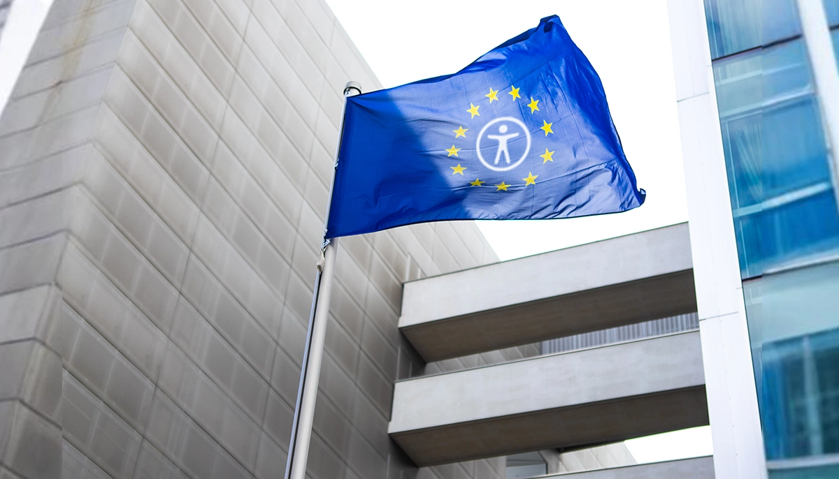 Un drapeau bleu ressemblant au drapeau de l'Union européenne, avec douze étoiles jaunes disposées en cercle et un symbole blanc d'accessibilité universelle au centre, flottant devant un bâtiment administratif ou gouvernemental moderne.