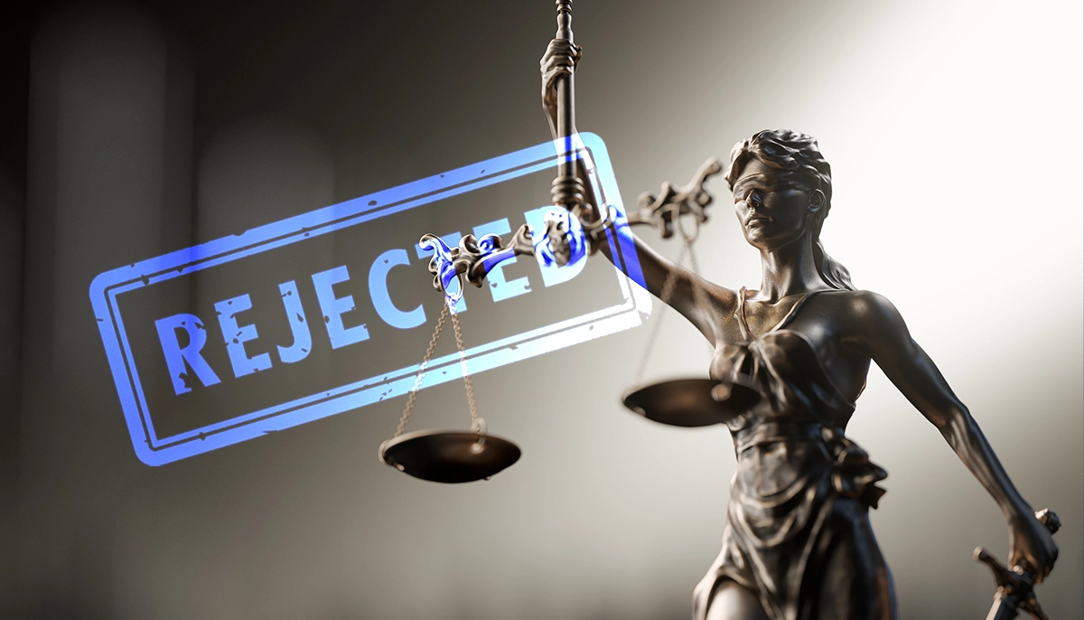 Statue de Dame Justice tenant une balance et portant un tampon « Rejeté » indiquant une décision judiciaire défavorable.
